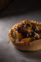 tart with salted caramel. Tart with nuts and caramel on a rustic background. Tartlets with dried fruits and nuts. Homemade tartlets with fruit and coffee. Dessert on a gray concrete table. Free space 