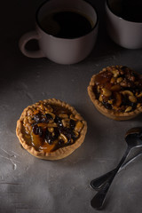 tart with salted caramel. Tart with nuts and caramel on a rustic background. Tartlets with dried fruits and nuts. Homemade tartlets with fruit and coffee. Dessert on a gray concrete table. Free space 