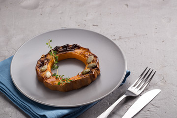 Pumpkin grill served on a plate. Baked pumpkin sliced rings with a knife, fork and napkin on a concrete table. Autumn dish. Halloween dish. Everyday autumn kitchen. Orange colors. space for text.  