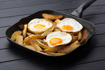 Breakfast in the pan. Fried potatoes with eggs in a skillet. Food bachelor. Cooked by a man. Hot and fresh. Homemade breakfast on black table. Fried eggs and sweet potato hash in cast iron skillet Fre