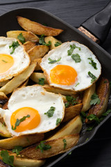Breakfast in the pan. Fried potatoes with eggs in a skillet. Food bachelor. Cooked by a man. Hot and fresh. Homemade breakfast on black table. Fried eggs and sweet potato hash in cast iron skillet Fre