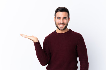 Young handsome man with beard over isolated white background holding copyspace imaginary on the palm to insert an ad