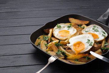 Breakfast in the pan. Fried potatoes with eggs in a skillet. Food bachelor. Cooked by a man. Hot and fresh. Homemade breakfast on black table. Fried eggs and sweet potato hash in cast iron skillet Fre