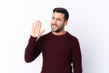 Young handsome man with beard over isolated white background saluting with hand with happy expression