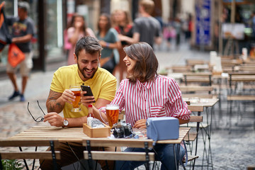 Man and  girl sitting at a cafe drinking beer and looking at pictures on a mobile phone.