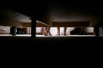 A loving couple is sitting on the couch and looking at each other. The photo was taken from the bottom through the bed and only legs and shoes are visible.