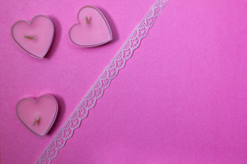 Candles in the shape of hearts on a pink background