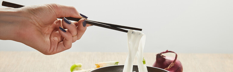 cropped view of woman eating rice noodles isolated on grey, panoramic shot
