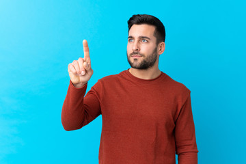 Young handsome man with beard over isolated blue background touching on transparent screen