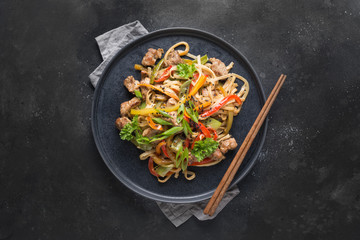 Udon stir-fry noodles with pork bowl and vegetables on black stone background. Asian cuisine.