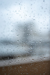 Window on a rainy day with small drops in it. Focus on the small drops with shallow depth of field and a visual of city buildings.