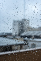Window on a rainy day with small drops in it. Focus on the small drops with shallow depth of field and a visual of city buildings.