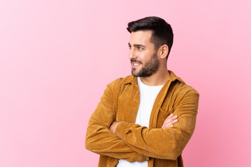 Young handsome man with beard wearing a corduroy jacket over pink background looking to the side