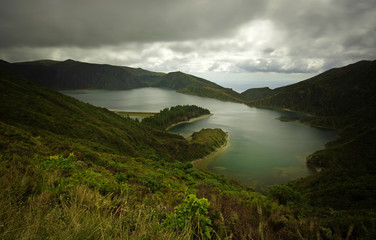 Foggy misty view of green lake in fog on Sao Miguel island, Azores. Cloudy sky, green water, fields and forests