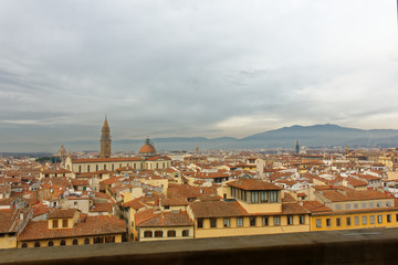 Fototapeta na wymiar Florence Firenze view from a rooftop during winter season. Really cloudy sky and lovely red and oranges roofs of the old and historic buildings from Tuscany.