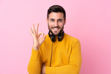 Young handsome man with earphones over isolated pink background showing ok sign with fingers