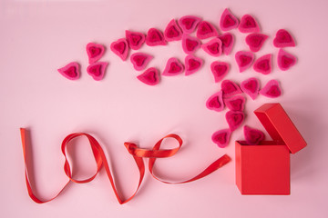 The word love laid out by a red ribbon next to a gift box and pink hearts