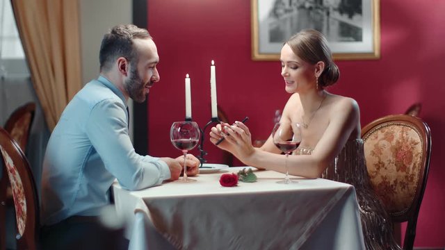 Couple laughing looking at screen of smartphone together at romantic date. Wide shot on RED camera