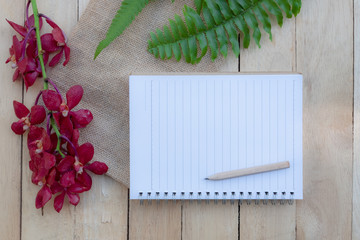 Blank paper note, pencil and vintage key on wooden table decorated with red orchid and green fern