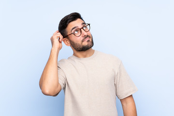 Young handsome man with beard over isolated blue background having doubts and with confuse face...
