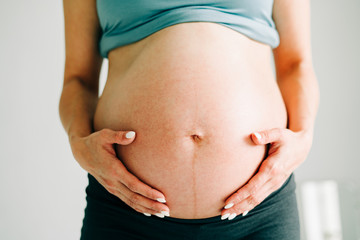 pregnant girl in sportswear hugs her bare belly in the Studio