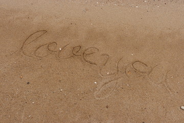 Handwriting  words "love you" on sand of beach.