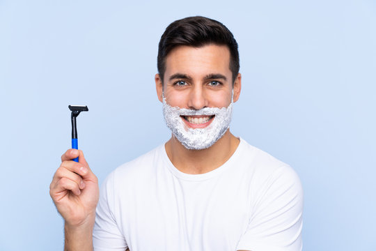 Young handsome man shaving his beard over isolated background smiling a lot