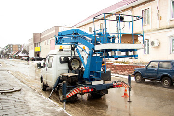 Fototapeta na wymiar A car lift stands on a city street. Machine getting ready to lift the cradle with a man
