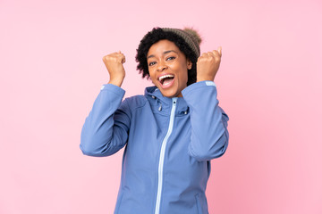 African american woman with winter hat over isolated pink background celebrating a victory