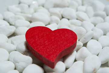 Red wooden heart on a white pebble background.