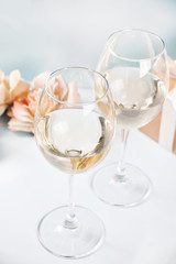Two glasses with white grape wine with roses and gift box on the background. Romantic dinner concept.