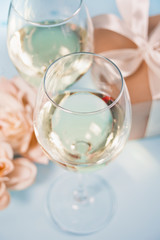 Two glasses with white grape wine with roses and gift box on the background. Romantic dinner concept.