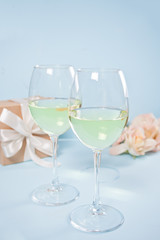 Two glasses with white grape wine with roses and gift box on the background. Romantic dinner concept.