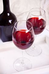 Two glasses with red grape wine with bottle on the background. Romantic dinner concept.