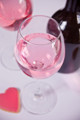 Two glasses with pink grape wine with heart shape cookie and bottle on the background. Romantic dinner concept.