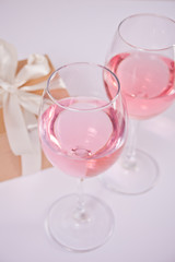 Two glasses with pink grape wine with flowers and gift box on the background. Romantic dinner concept.
