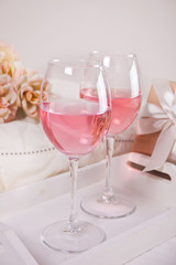 Two glasses with pink grape wine with flowers and gift box on the background. Romantic dinner concept.