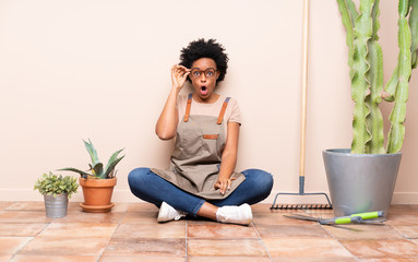 Gardener woman sitting on the floor with glasses and surprised