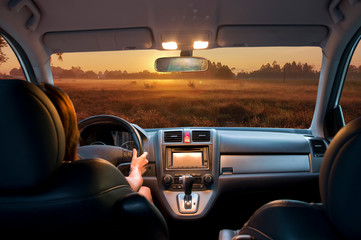 view from car inside with part of interior gps screen with driver female hand on the steering wheel during sun on morning mist and meadow - 321517919