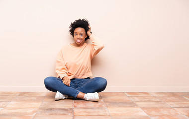 African american woman sitting on the floor with an expression of frustration and not understanding