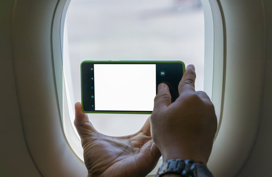Holding a smartphone with a blank screen to take pictures by the window on an airplane