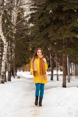 Young beautiful woman in yellow coat walking winter park