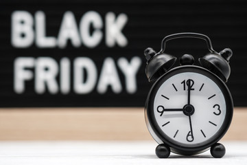 black analog alarm clock on the background of the English text black Friday. concept for the start...