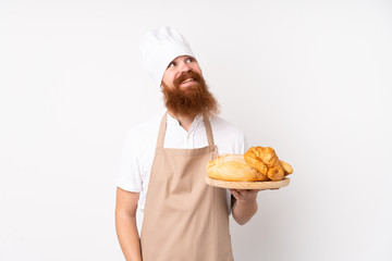 Redhead man in chef uniform. Male baker holding a table with several breads looking up while smiling