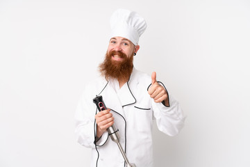 Redhead man using hand blender over isolated white background giving a thumbs up gesture