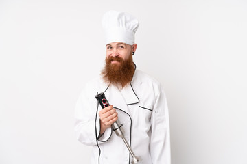 Redhead man using hand blender over isolated white background having doubts and with confuse face expression