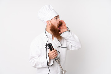 Redhead man using hand blender over isolated white background shouting with mouth wide open