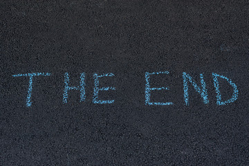 Word THE END is written in chalk on the asphalt. Inscription on pavement.
