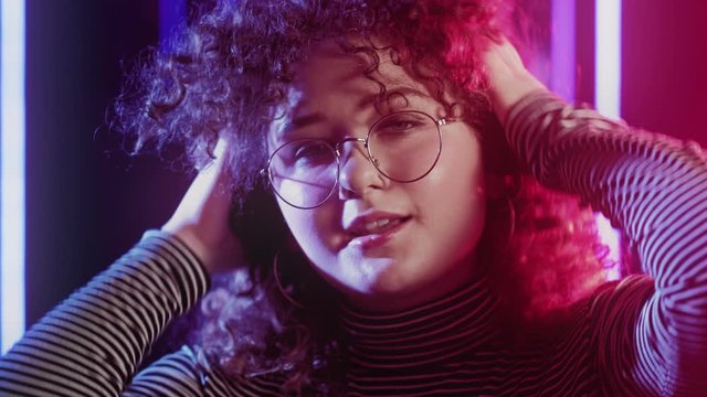 80s style girl portrait. Youth beauty. Woman in eyeglasses touching curly hair in blue pink neon glow.