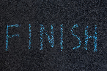 Fototapeta na wymiar Text FINISH underfoot. Black asphalt with chalk inscription. The end concept